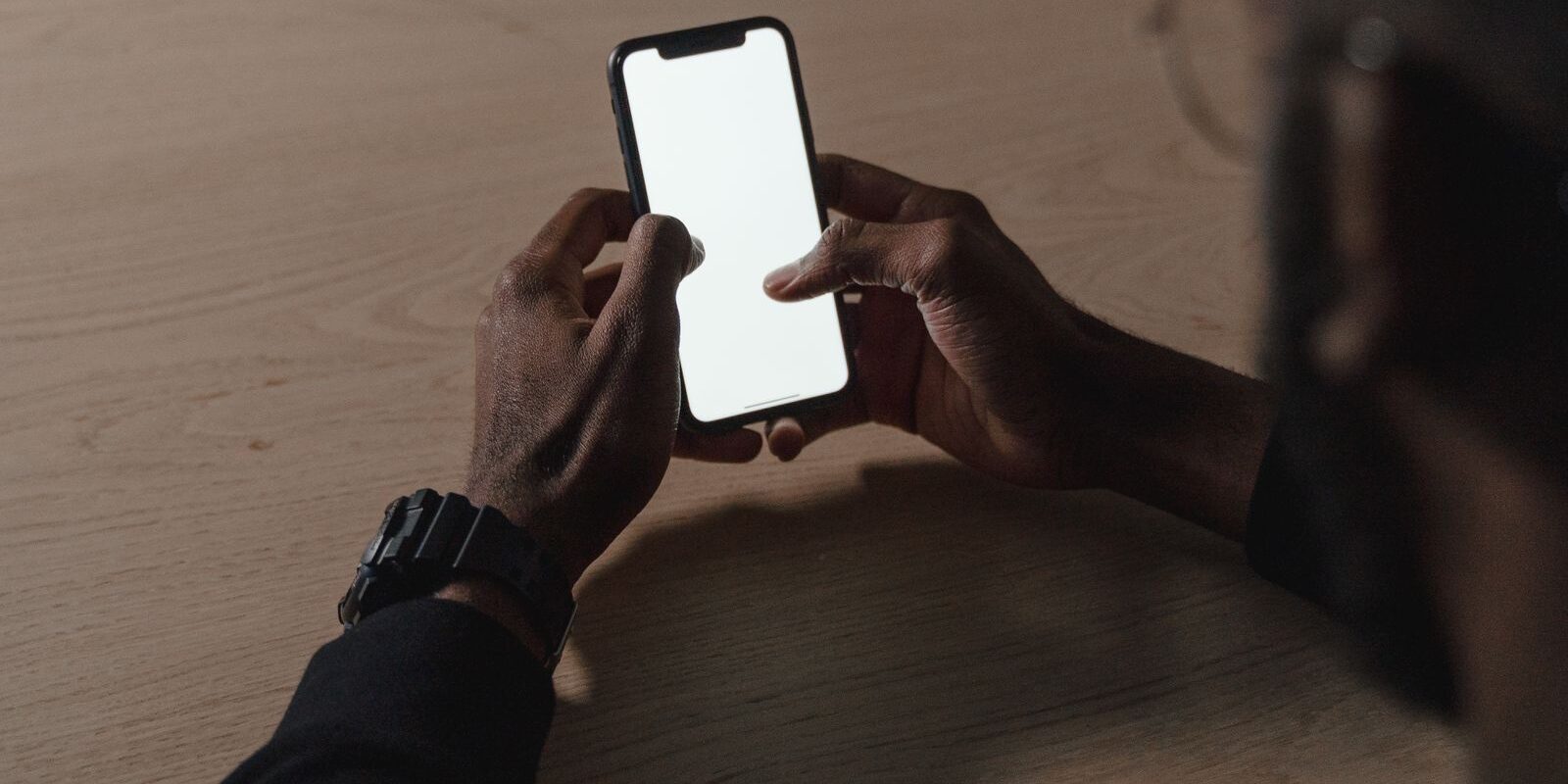 Manos de una persona sosteniendo un celular con la pantalla en blanco sobre una mesa de madera