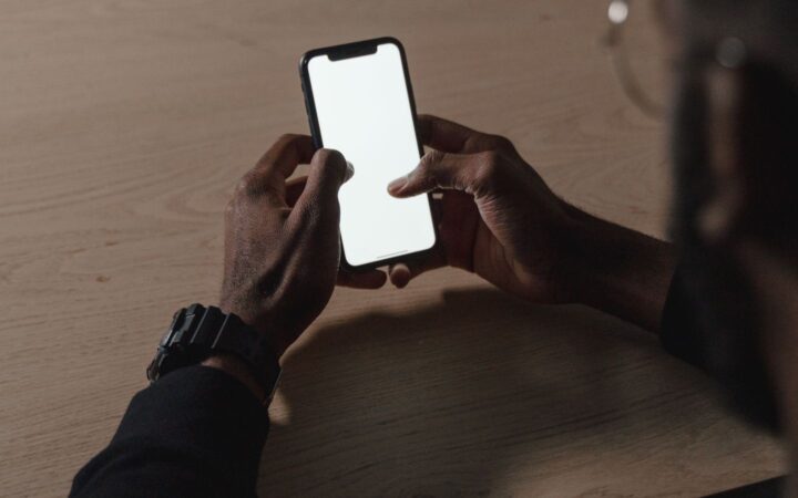 Manos de una persona sosteniendo un celular con la pantalla en blanco sobre una mesa de madera
