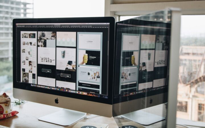Dos monitores sobre un escritorio mostrando el diseño de un sitio web