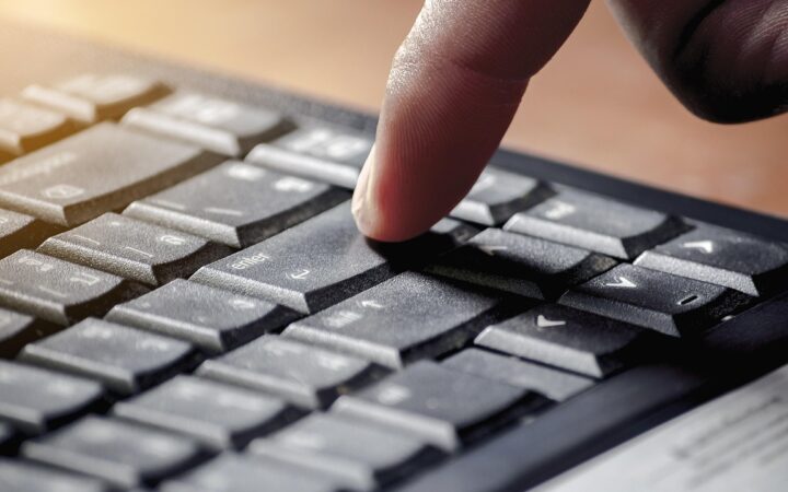 Dedo de una persona a punto de presionar la tecla Enter de un teclado negro