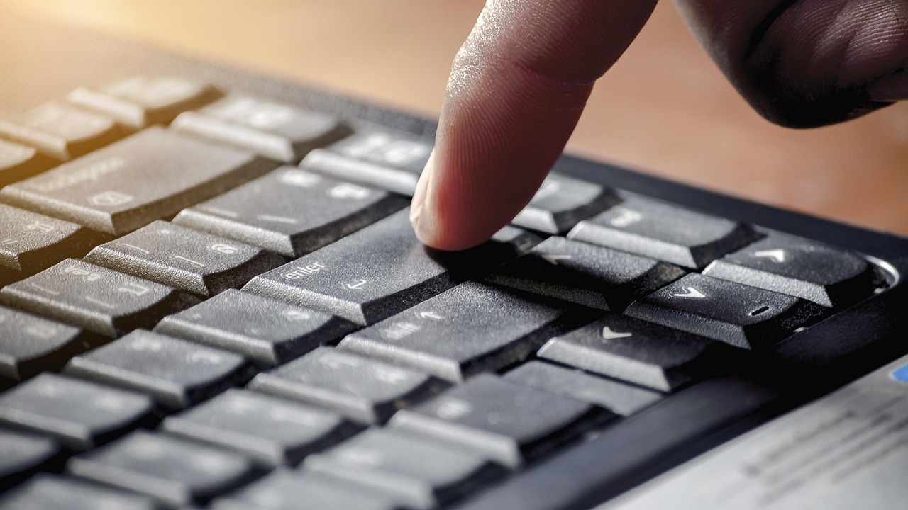 Dedo de una persona a punto de presionar la tecla Enter de un teclado negro