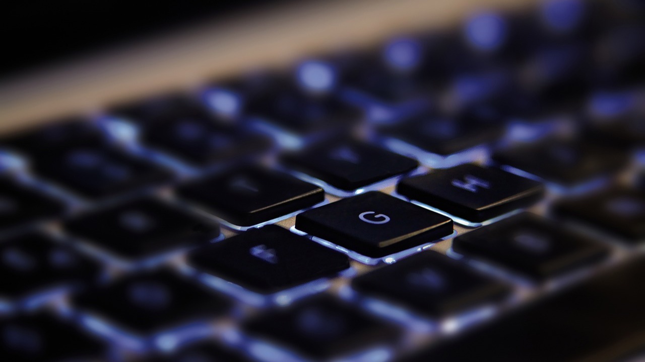 Teclado de computadora con retroiluminación azul visto de cerca, con la tecla G enfocada