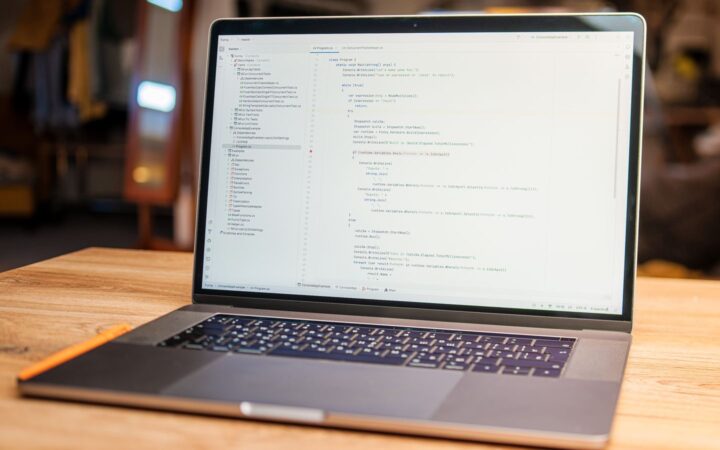 Laptop abierta con código en pantalla sobre un escritorio de madera en un espacio de trabajo con poca luz
