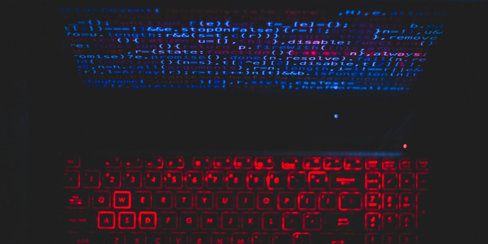 Laptop en un cuarto oscuro con el teclado iluminado en rojo y líneas de código reflejadas en azul