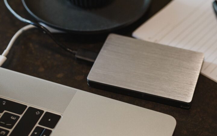 Disco duro externo plateado conectado con un cable a una laptop sobre un escritorio oscuro