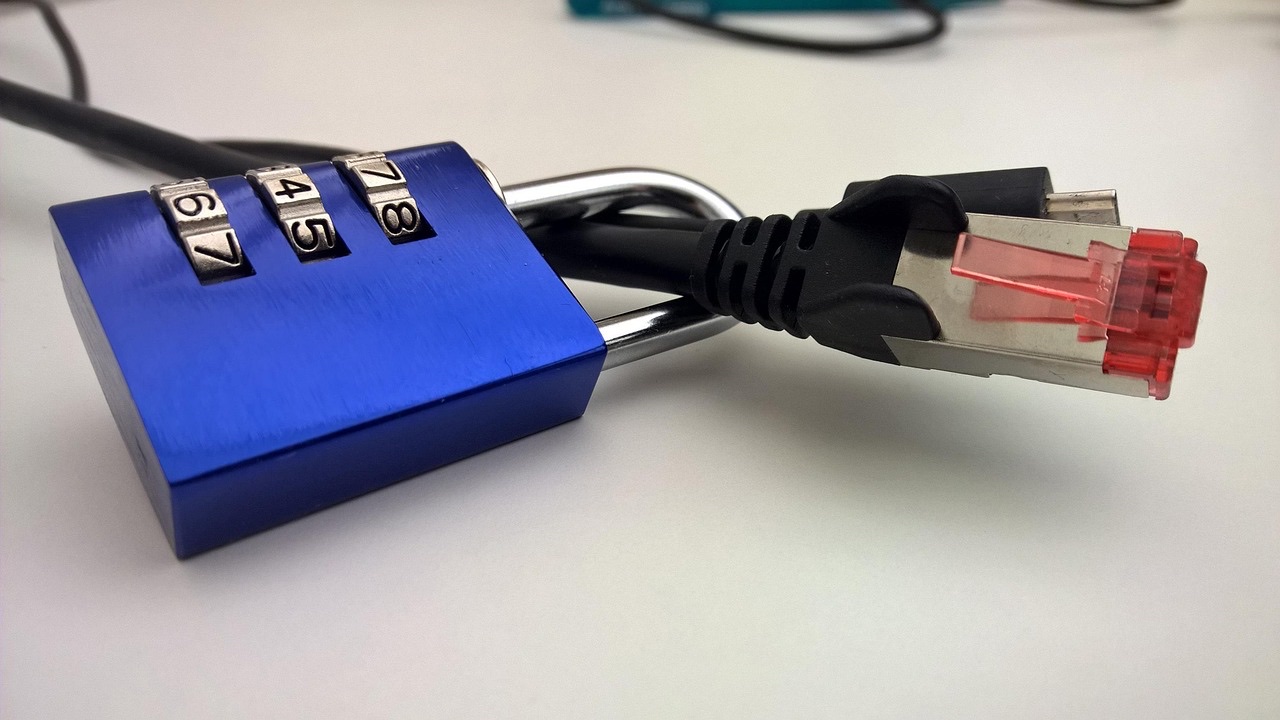 Candado azul de combinación junto a un cable de red sobre una mesa blanca