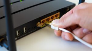 Mano conectando un cable de red blanco en la parte trasera de un router negro con antenas