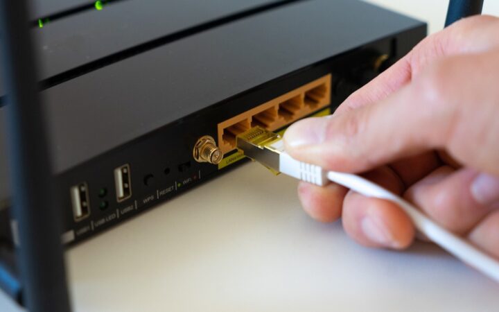 Mano conectando un cable de red blanco en la parte trasera de un router negro con antenas