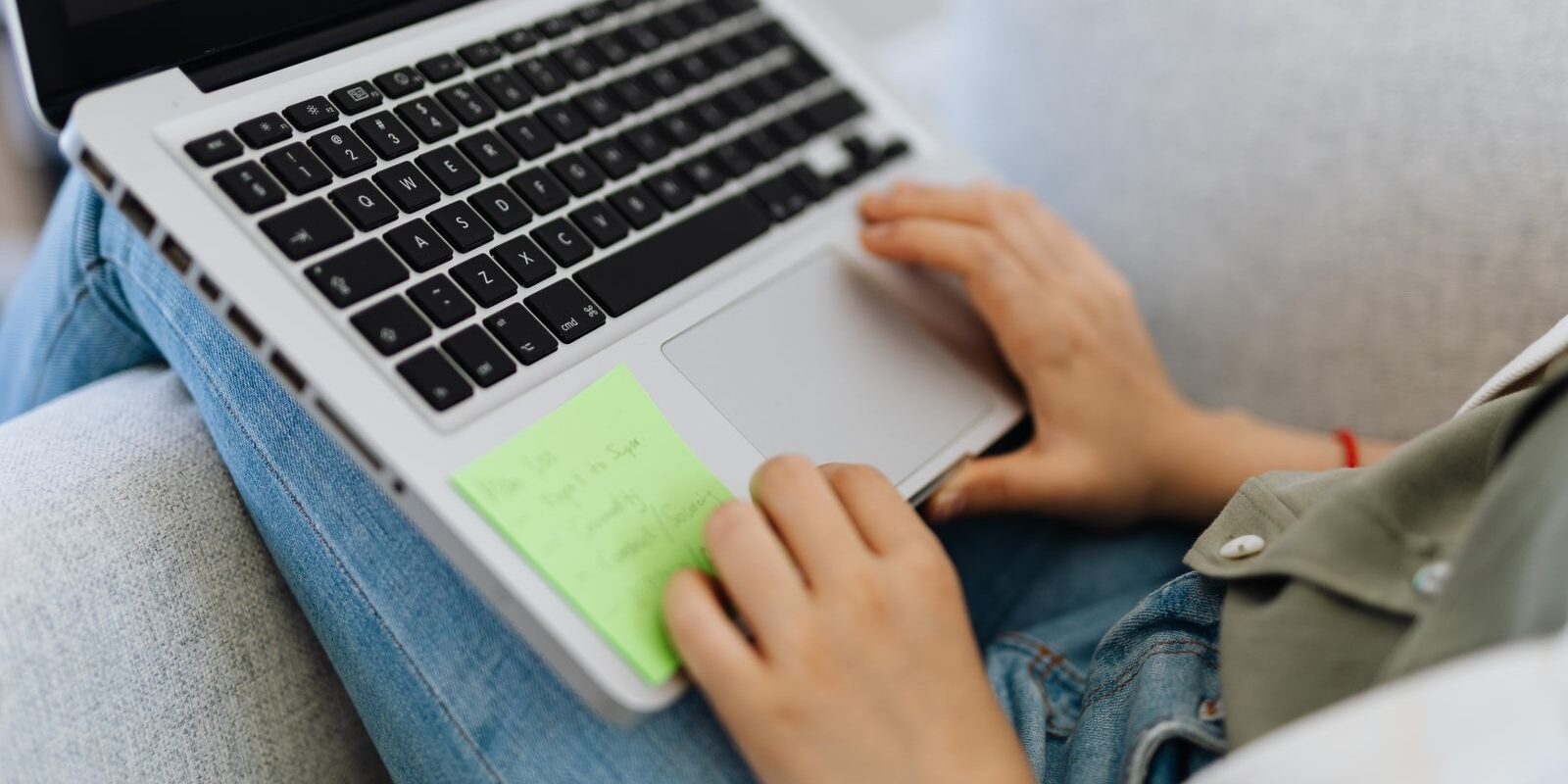 Manos de una persona usando el touchpad de una laptop apoyada sobre sus piernas en un sillón