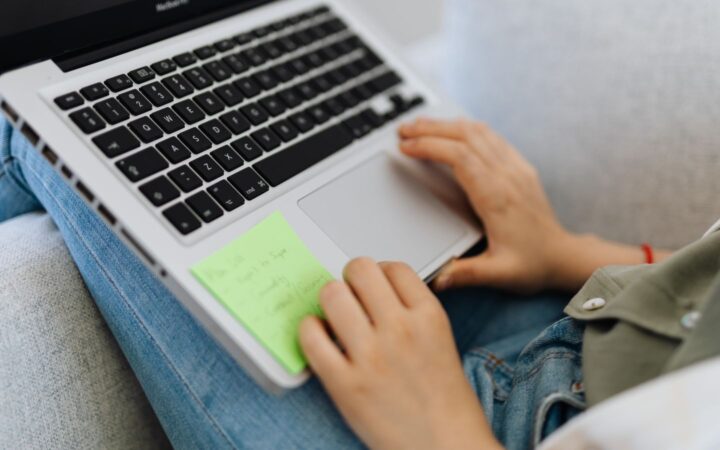 Manos de una persona usando el touchpad de una laptop apoyada sobre sus piernas en un sillón