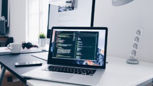 Laptop con un editor de código abierto sobre un escritorio blanco junto a una taza de café y unos audífonos