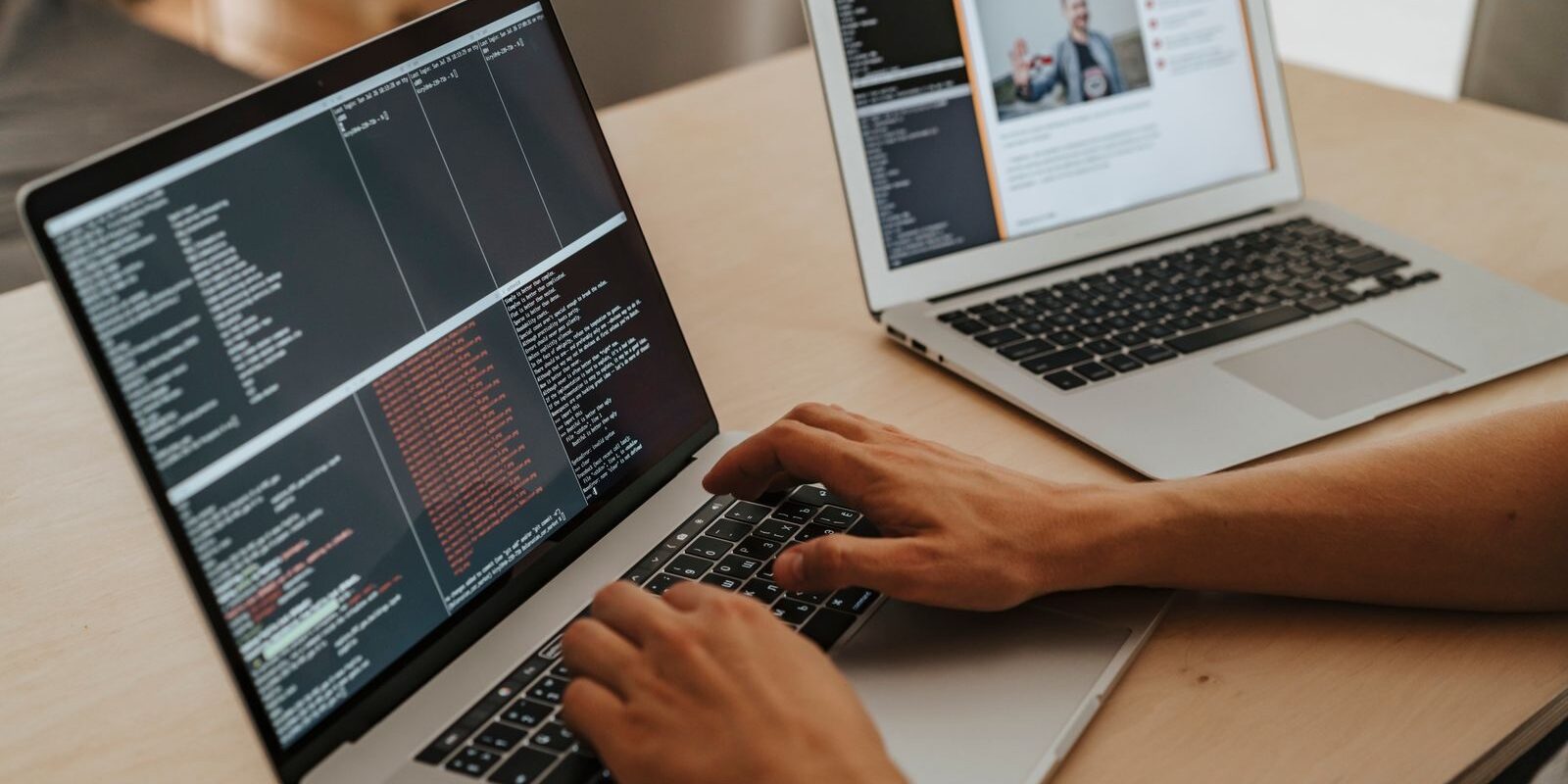 Manos de una persona escribiendo en una laptop con una terminal abierta junto a otra laptop sobre una mesa de madera