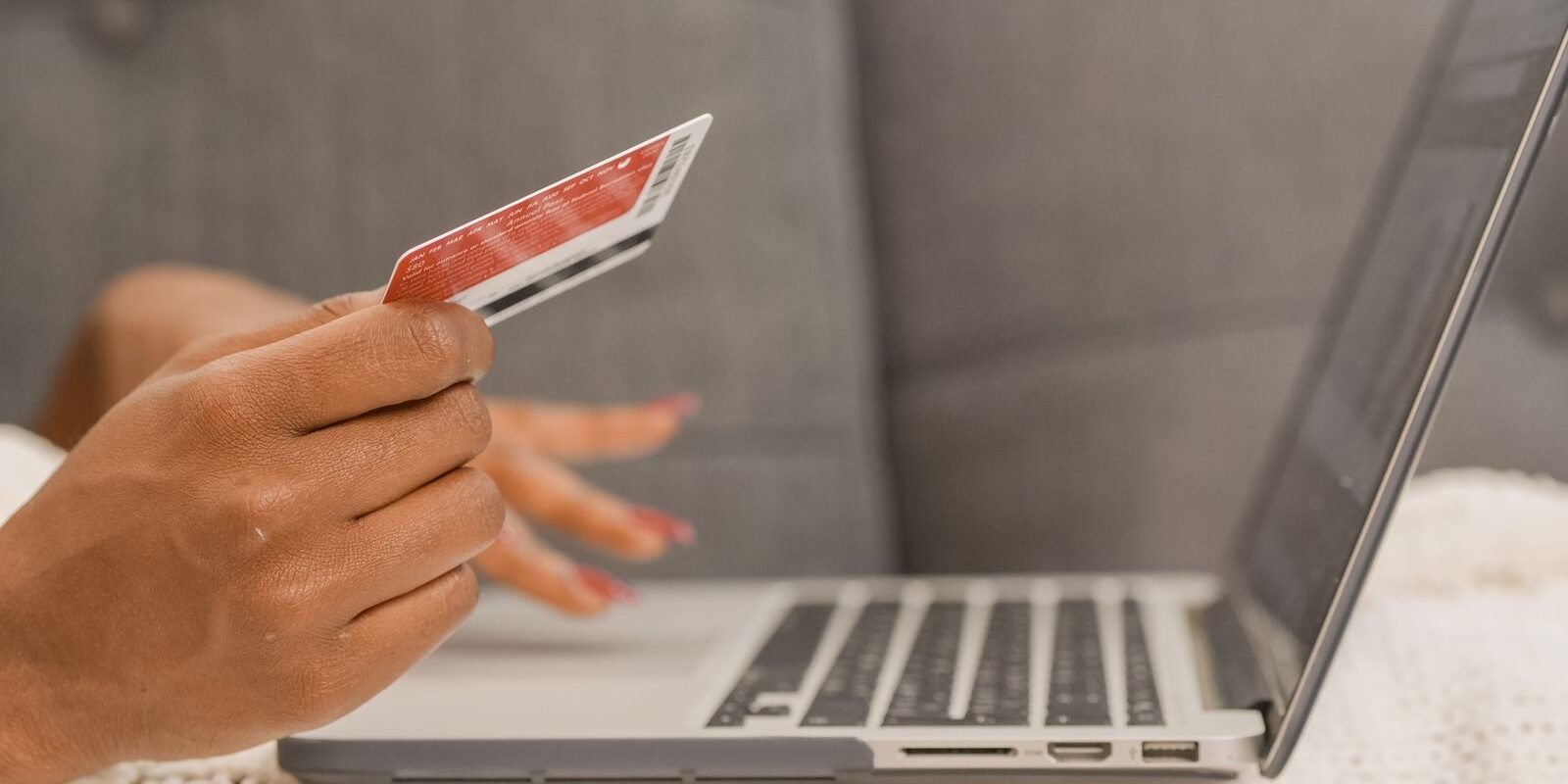 Persona con una tarjeta bancaria en la mano frente a una laptop abierta