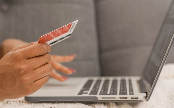 Persona con una tarjeta bancaria en la mano frente a una laptop abierta