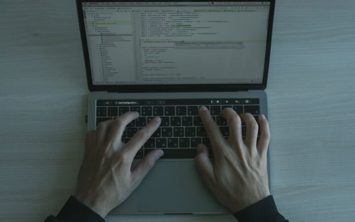 Manos de una persona escribiendo en el teclado de una laptop con código en la pantalla