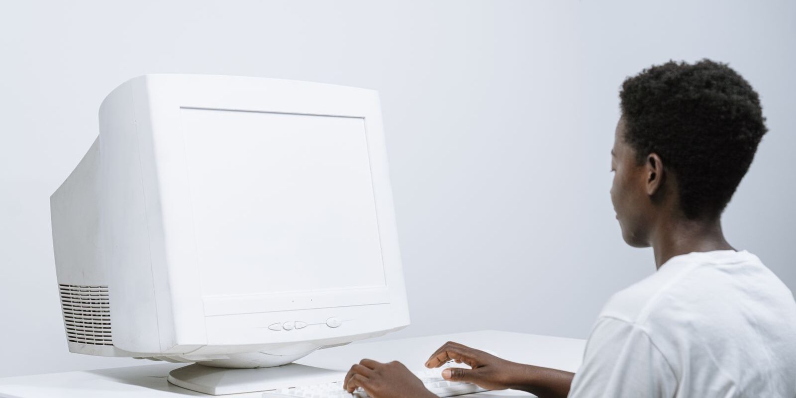 Una persona escribe en el teclado de una computadora de escritorio blanca con monitor clásico
