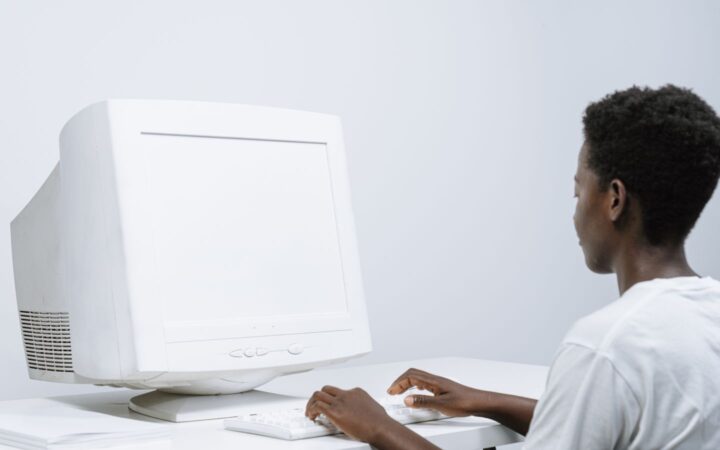 Una persona escribe en el teclado de una computadora de escritorio blanca con monitor clásico