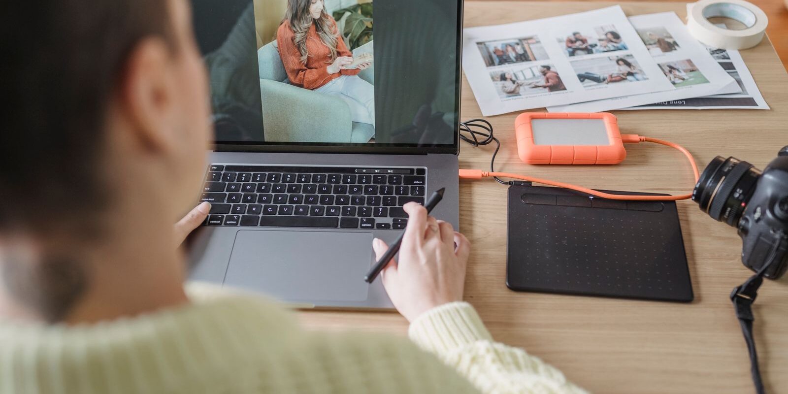 Persona revisando una fotografía en su laptop junto a una tableta gráfica y una cámara