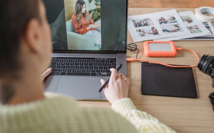 Persona revisando una fotografía en su laptop junto a una tableta gráfica y una cámara