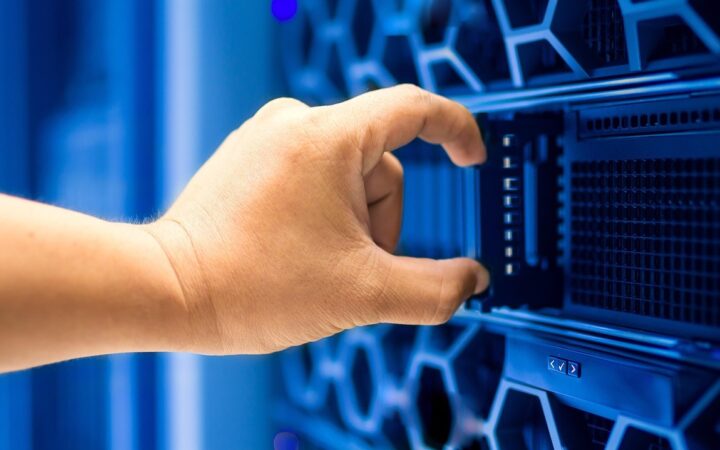 Mano de una persona tomando un servidor de un rack iluminado en azul dentro de un centro de datos