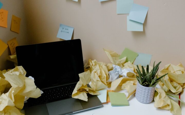 Laptop sobre un escritorio rodeada de bolas de papel arrugado y notas adhesivas pegadas en la pared