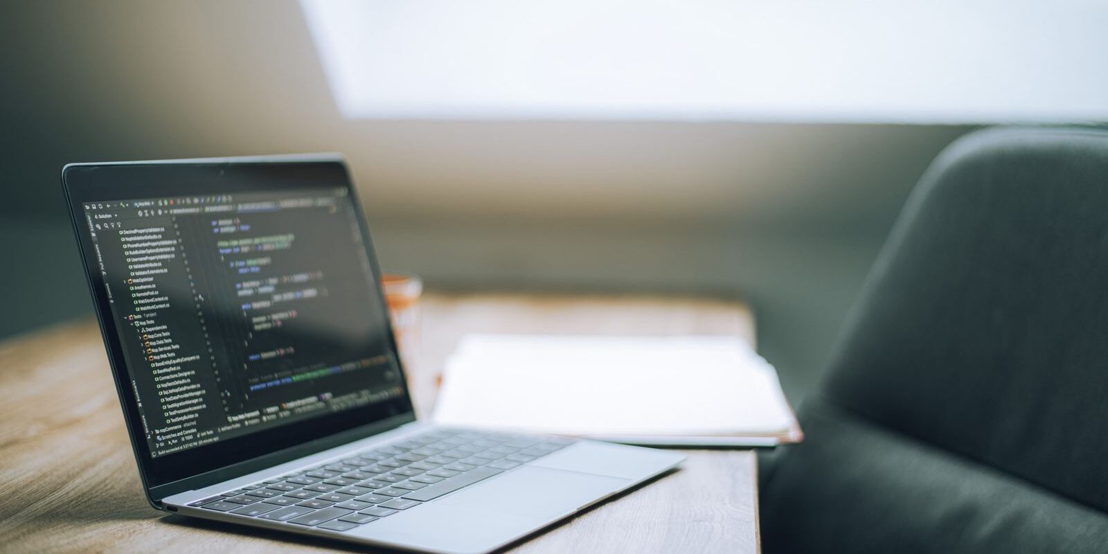 Laptop abierta con código en la pantalla sobre una mesa de madera junto a un sillón