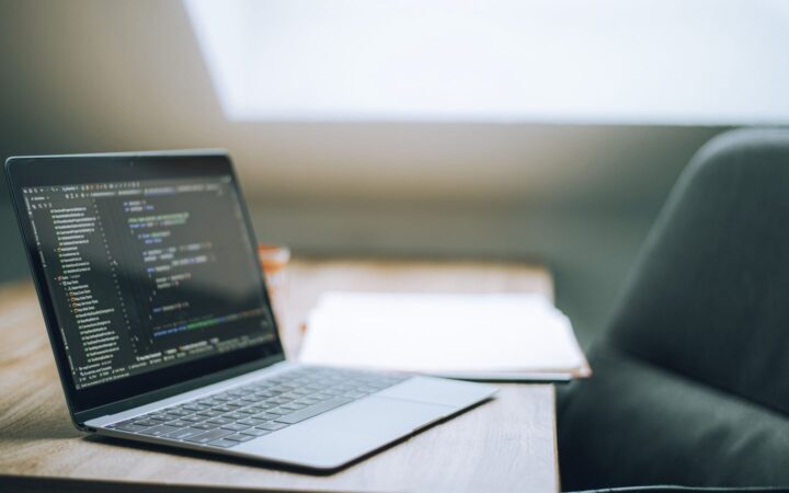 Laptop abierta con código en la pantalla sobre una mesa de madera junto a un sillón
