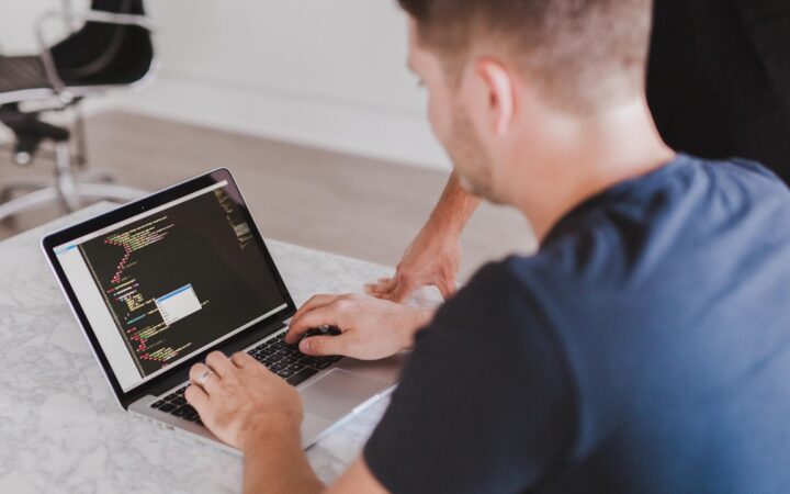 Manos de una persona escribiendo código en una laptop sobre una mesa de mármol