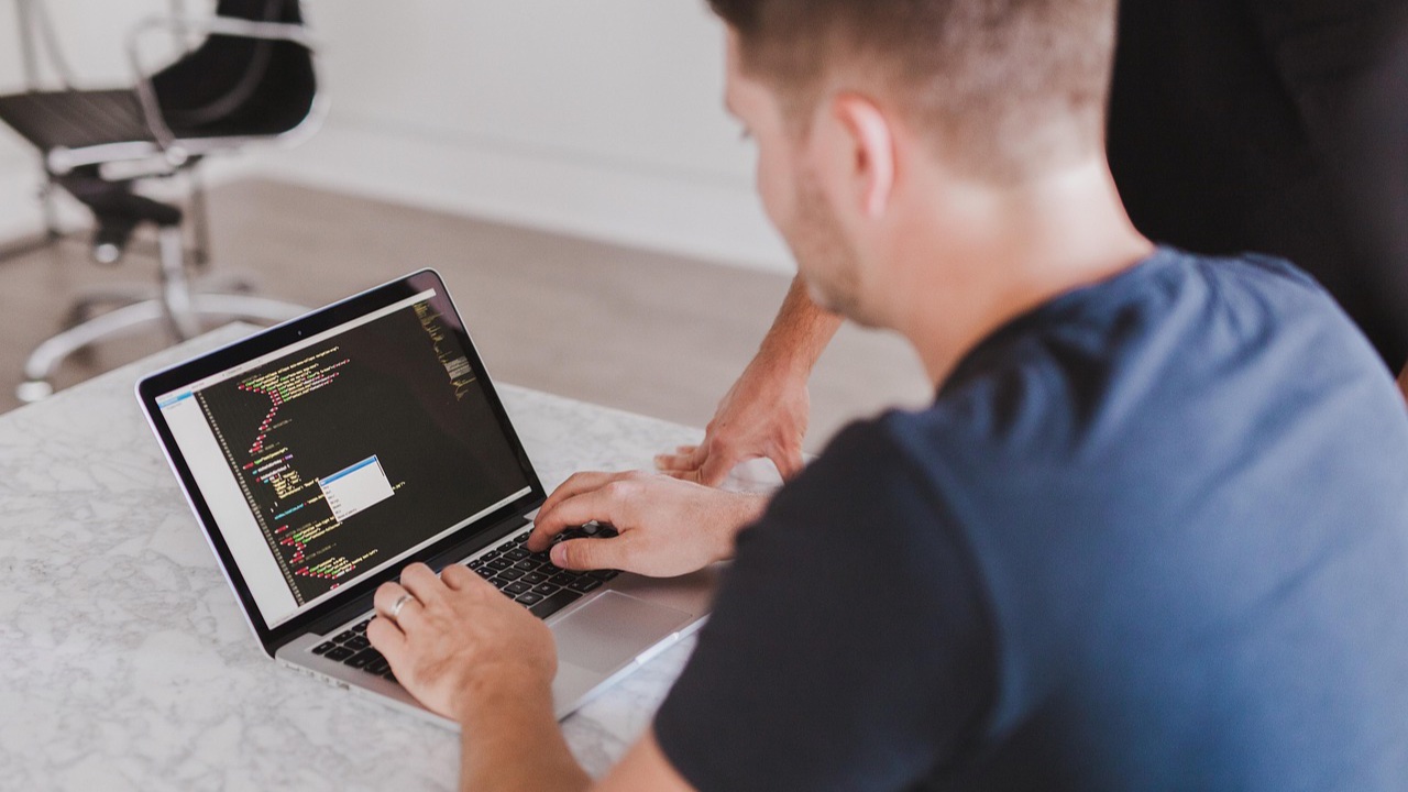 Manos de una persona escribiendo código en una laptop sobre una mesa de mármol