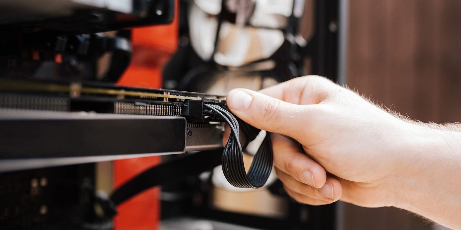 Mano conectando un cable de corriente a una tarjeta gráfica dentro de una computadora de escritorio