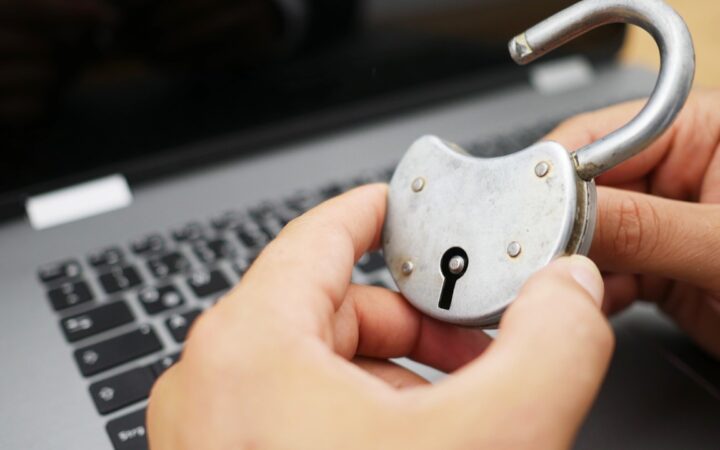 Manos sosteniendo un candado abierto frente al teclado de una laptop