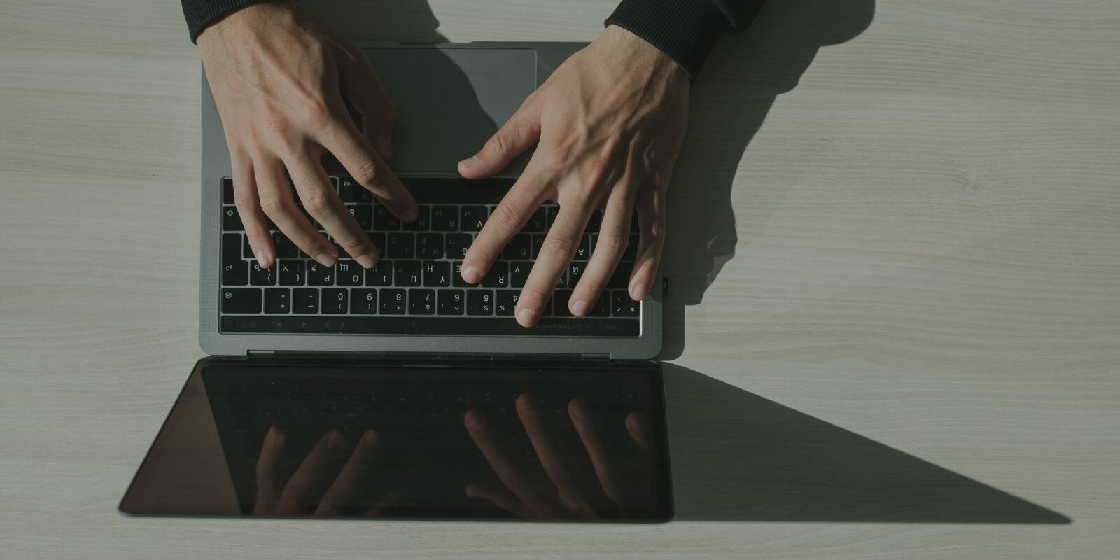 Manos de una persona escribiendo en una laptop sobre un escritorio claro, vista desde arriba