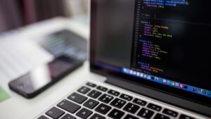 Laptop abierta con código en la pantalla junto a un celular sobre un escritorio