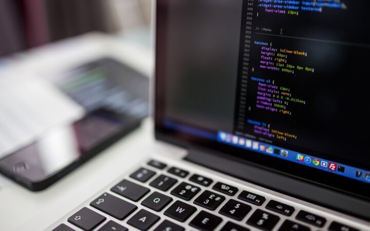 Laptop abierta con código en la pantalla junto a un celular sobre un escritorio