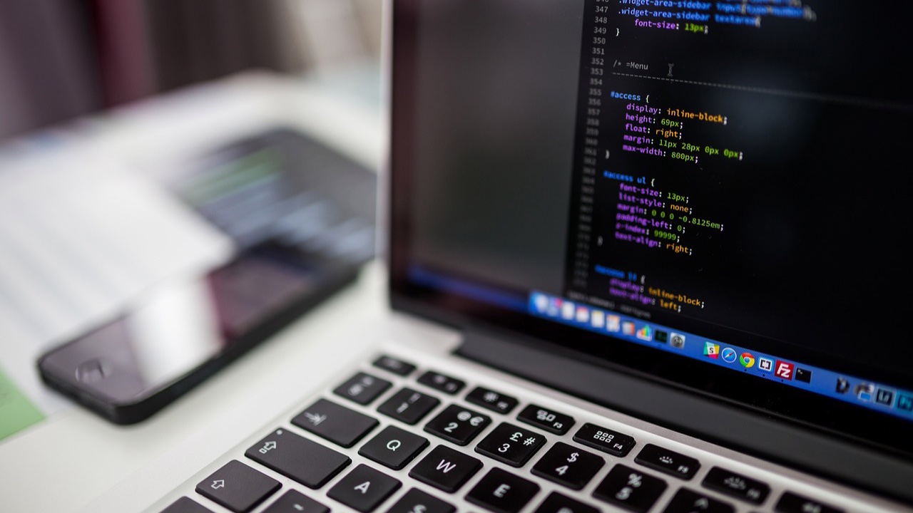 Laptop abierta con código en la pantalla junto a un celular sobre un escritorio