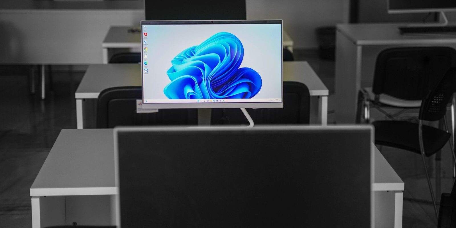 Monitor encendido con fondo de pantalla azul en una oficina con escritorios vacíos