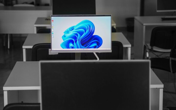 Monitor encendido con fondo de pantalla azul en una oficina con escritorios vacíos