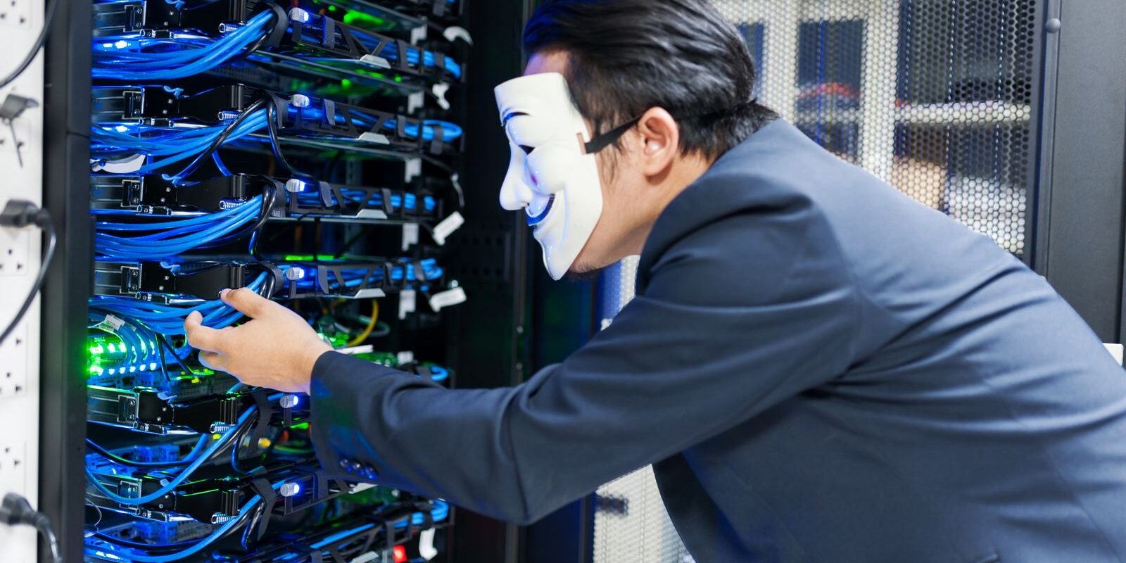 Persona con traje y máscara blanca manipulando cables de un rack de servidores en un centro de datos
