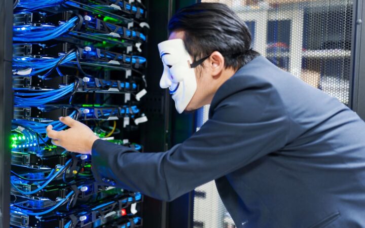 Persona con traje y máscara blanca manipulando cables de un rack de servidores en un centro de datos